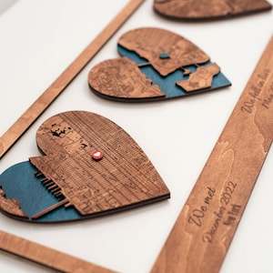 Puede incluir: Arte de mapa en forma de coraz&oacute;n de madera con un marco. El arte presenta tres mapas en forma de coraz&oacute;n con un fondo azul. El marco tiene el texto "We met December 2022 New York" y "We fell in love May 2023".