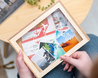 Peut inclure: Une boîte à ombre en bois avec un motif de carte du monde. La boîte contient divers objets sur le thème du voyage, notamment des photos, des billets et des cartes postales.