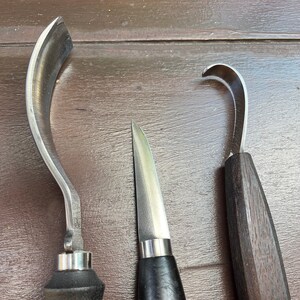 May include: Three wood carving tools with wooden handles. The tools have different shaped blades, including a curved blade, a straight blade, and a hook blade.