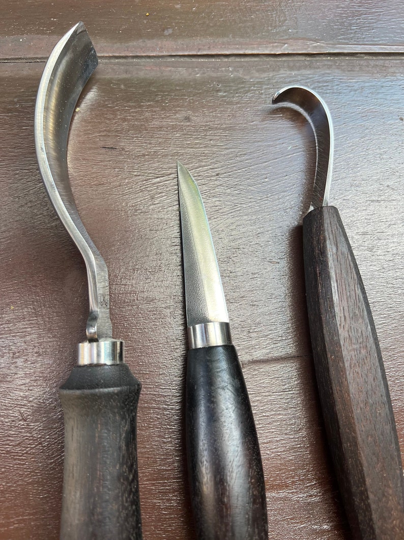 May include: Three wood carving tools with wooden handles. The tools have different shaped blades, including a curved blade, a straight blade, and a hook blade.
