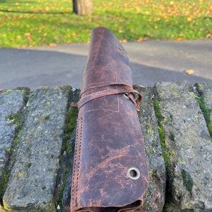 May include: A brown leather roll with stitching and metal eyelets. The roll is rolled up and tied with a leather strap.