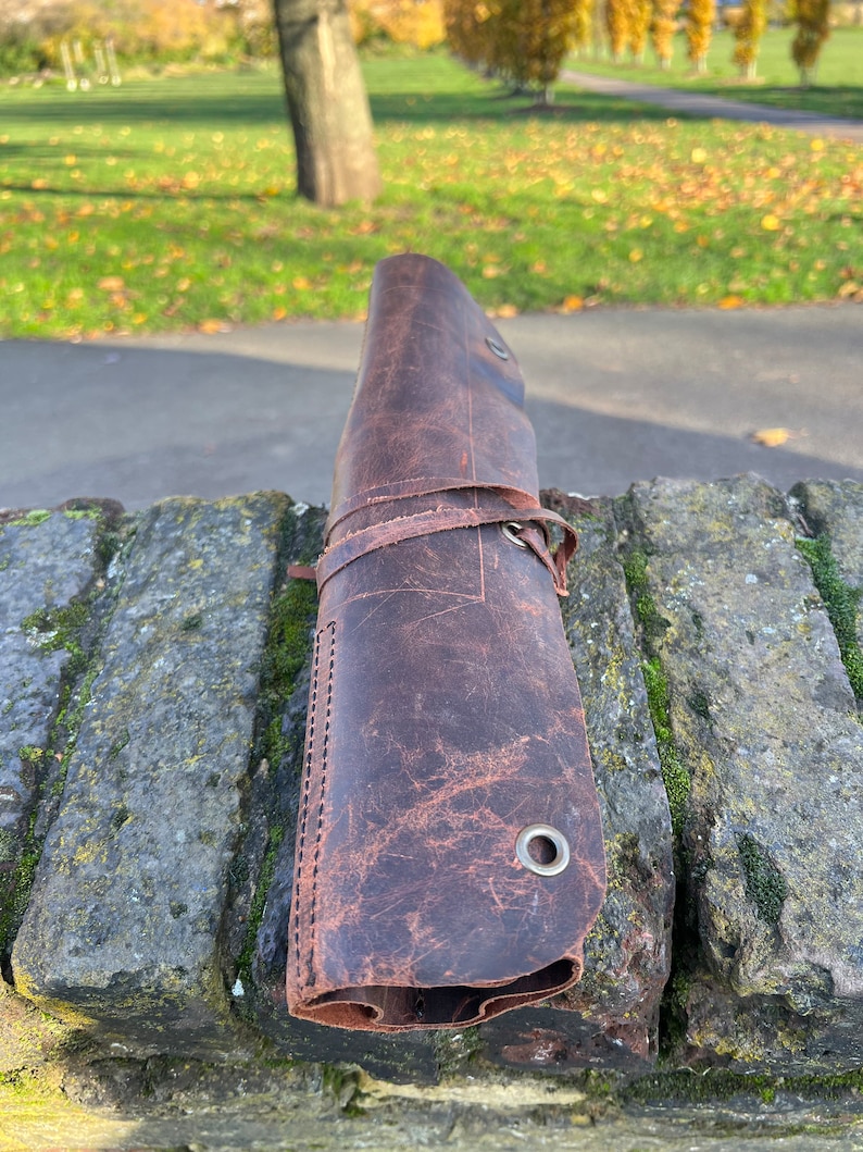 May include: A brown leather roll with stitching and metal eyelets. The roll is rolled up and tied with a leather strap.