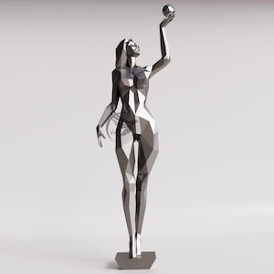 Op de afbeelding: Een geometrisch, zilverkleurig beeld van een vrouw die een bol boven haar hoofd houdt. De figuur heeft een modern, hoekig ontwerp en staat op een grijze, zeshoekige basis. Het beeld staat tegen een effen witte achtergrond.