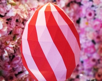 May include: A large, red and pink papercraft egg with a geometric design. The egg is sitting on a mirrored surface.