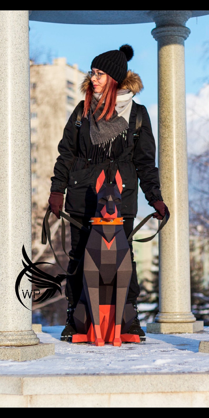 Peut inclure: Une femme portant un manteau d'hiver noir, un bonnet noir en tricot avec un pompon et une &eacute;charpe grise prom&egrave;ne un Doberman Pinscher en papier noir et rouge.