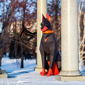 Peut inclure: Sculpture en papier d'un Dobermann Pinscher noir et orange assis devant des colonnes blanches. Le chien porte un collier en cuir marron.