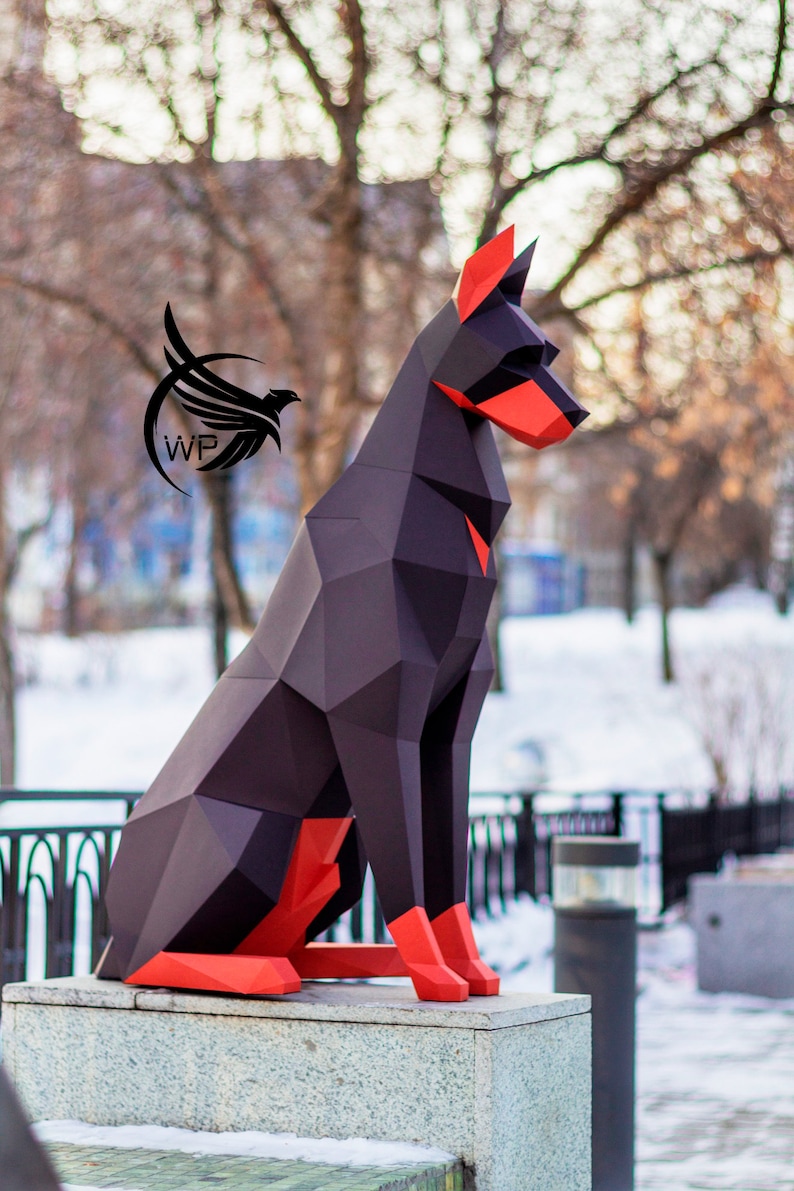 Peut inclure: Un mod&egrave;le de chien en origami en papier noir et rouge assis sur un pi&eacute;destal en pierre grise. Le chien est fait de papier pli&eacute; et a un design g&eacute;om&eacute;trique.