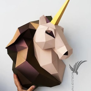 Puede incluir: Una escultura de cabeza de unicornio de papel con un cuerno dorado, papel marrón y rosa y un diseño geométrico. La escultura está montada en una pared blanca.