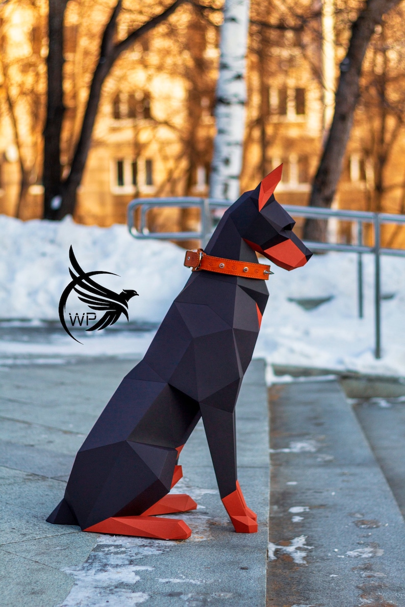Peut inclure: Un chien origami Doberman Pinscher noir et orange assis sur un escalier en b&eacute;ton. Le chien porte un collier en cuir marron avec des clous argent&eacute;s.