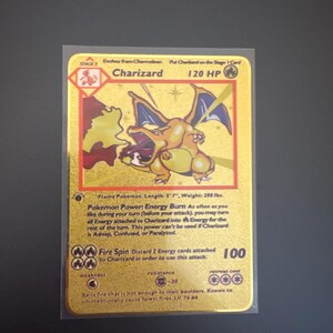 May include: A gold-coloured Charizard trading card featuring the character in a dynamic pose with wings spread. The card displays 120 HP, the text 'Flame Pokemon', 'Energy Burn' power, and 'Fire Spin' attack details. It is a Stage 2 card.