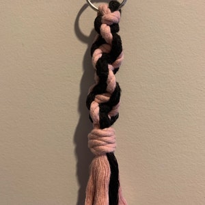 May include: A pink and black braided rope keychain with a tassel. The keychain is attached to a silver key ring.