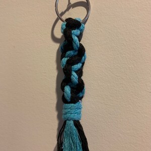 May include: A black and teal blue braided rope keychain with a silver key ring. The keychain has a tassel at the end.