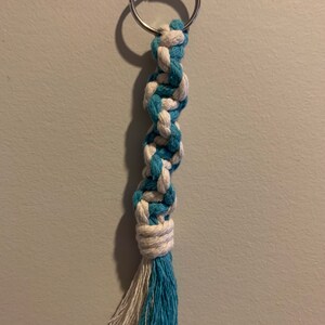 May include: A blue and white braided rope keychain with a silver key ring. The rope is tied into a knot at the bottom and has a tassel.