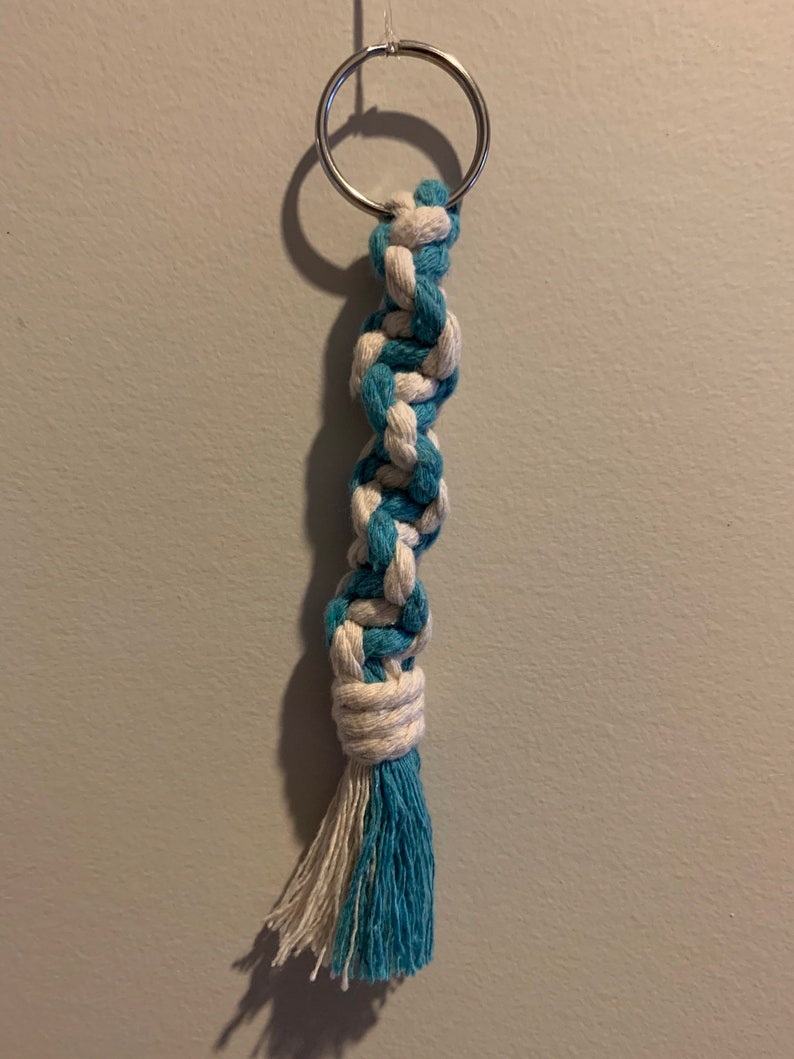 May include: A blue and white braided rope keychain with a silver key ring. The rope is tied into a knot at the bottom and has a tassel.