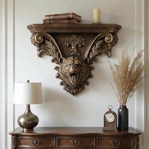 May include: A decorative wall shelf in dark brown with a carved bear head. The shelf has gold-coloured trim and holds books and a candle. It is mounted on a white wall above a wooden dresser. The shelf's dimensions are not visible.