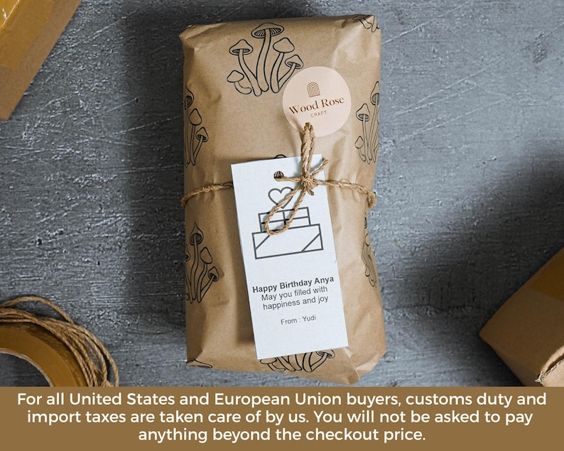 May include: A rectangular package wrapped in brown paper with a black mushroom pattern, secured with twine. A round Wood Rose Craft sticker and a white gift tag are attached. The tag features a heart icon and the text: Happy Birthday Anya.
