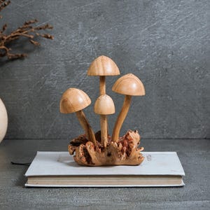 Pu&ograve; includere: Una scultura decorativa composta da quattro funghi in legno marrone chiaro, con superfici lisce e altezze variabili, che emergono da un'unica base in legno nodoso e strutturato. I cappelli sono arrotondati e levigati, con steli sottili.