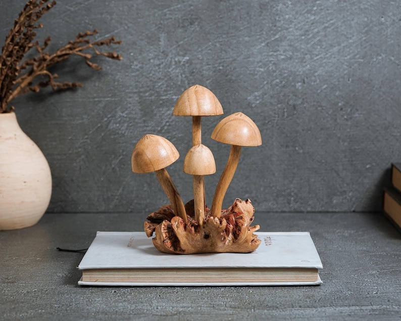 Pu&ograve; includere: Una scultura decorativa composta da quattro funghi in legno marrone chiaro, con superfici lisce e altezze variabili, che emergono da un'unica base in legno nodoso e strutturato. I cappelli sono arrotondati e levigati, con steli sottili.