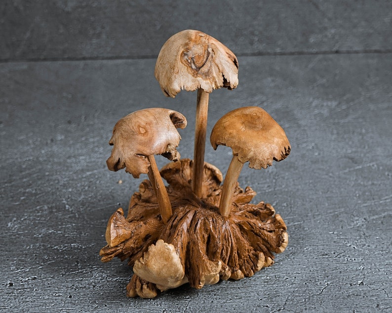 May include: A wooden sculpture of three mushrooms with brown caps and stems. The mushrooms are clustered together on a base of carved wood.