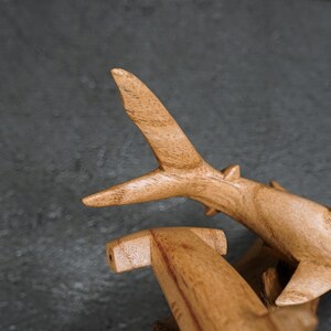 May include: Wooden shark sculptures with a natural wood grain finish. The sculptures are detailed with fins and a hammerhead shape. The sharks are set against a dark gray background.