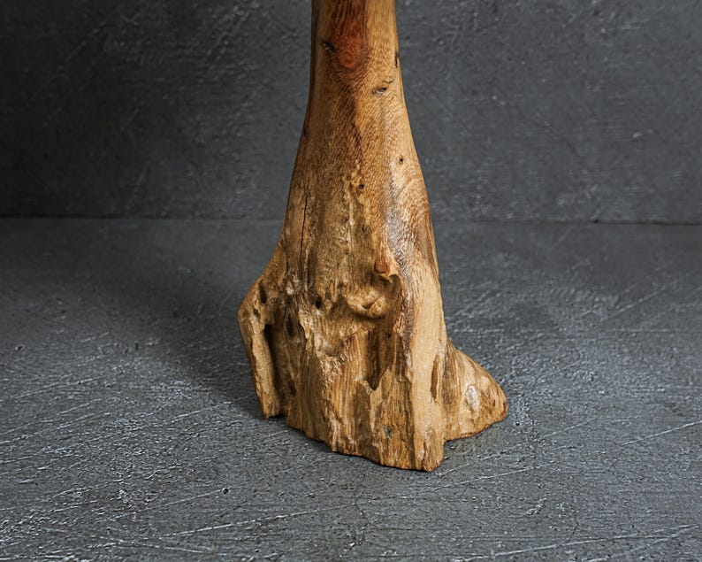 May include: A vertical piece of natural light brown wood with a rough, textured base and a smoother, cylindrical upper section. The wood displays visible grain patterns, knots, and organic irregularities throughout its surface structure.
