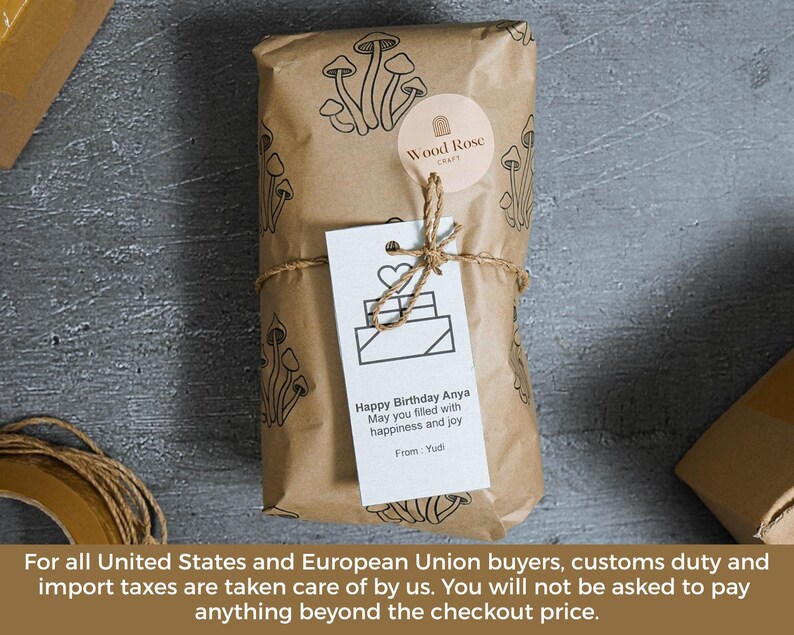 May include: A rectangular package wrapped in brown paper with a black mushroom pattern, secured with twine. A round Wood Rose Craft sticker and a white gift tag are attached. The tag features a heart icon and the text: Happy Birthday Anya.