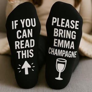 May include: A pair of black socks with white text. One sock says "If you can read this" with an arrow pointing up. The other sock says "Please bring Emma champagne" with a glass of champagne graphic.