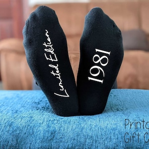 Pode incluir: Um par de meias pretas com texto branco. Uma meia diz "Edição limitada" e a outra diz "1981".