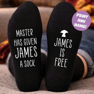 Può includere: Calzini neri con testo bianco. Uno dice "MASTER HAS GIVEN JAMES A SOCK". L'altro dice "JAMES IS FREE" con una grafica. Un cerchio viola dice "PRINT ANY NAME!"