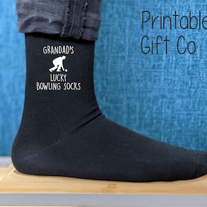 May include: Black socks with a white design that says "Grandad's Lucky Bowling Socks" and a silhouette of a person bowling.