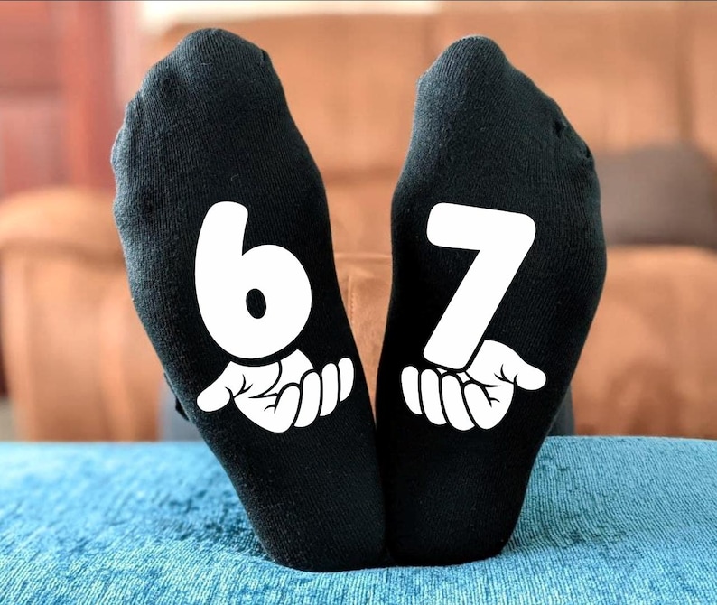 May include: Black socks with the numbers 6 and 7 printed in white on the soles. Each number is accompanied by a white graphic of a hand. The socks are displayed on a blue surface.