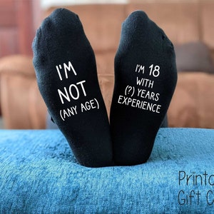 May include: A pair of black socks with white text. One sock says "I'm not (any age)" and the other says "I'm 18 with (?) years experience".