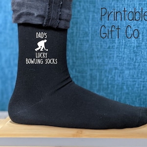Puede incluir: Calcetines negros con un diseño blanco que dice "Dad's Lucky Bowling Socks" y una silueta de una persona jugando a los bolos.