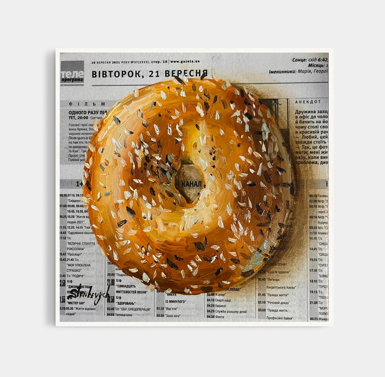 May include: A painting of a bagel with sesame seeds on top. The bagel is painted on a newspaper with the text "ВІВТОРОК, 21 ВЕРЕСНЯ" visible.