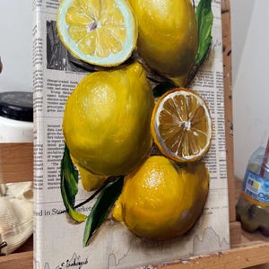 May include: A painting on canvas featuring several bright yellow lemons and two sliced lemon halves with visible segments. The fruit is depicted with green leaves against a background of printed newspaper text and financial market data.
