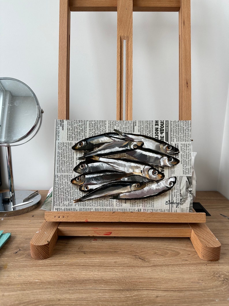 May include: A painting of a group of silver fish on a newspaper background. The newspaper headline reads "Zlodb-31 NE MO" and the artist's signature is visible in the bottom right corner.