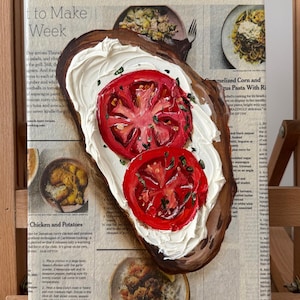 May include: A painting of a slice of bread with white cream cheese and two red tomato slices on top. The painting is on a canvas with a newspaper background. The newspaper text includes the words "Original are sold. Newspaper will be another" and a recipe for "Chicken and Potatoes".