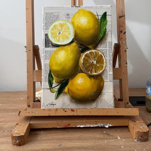 May include: A rectangular canvas painting featuring a cluster of bright yellow lemons, including two whole lemons and two sliced halves, accented with dark green leaves. The artwork is layered over a background of printed newspaper text.