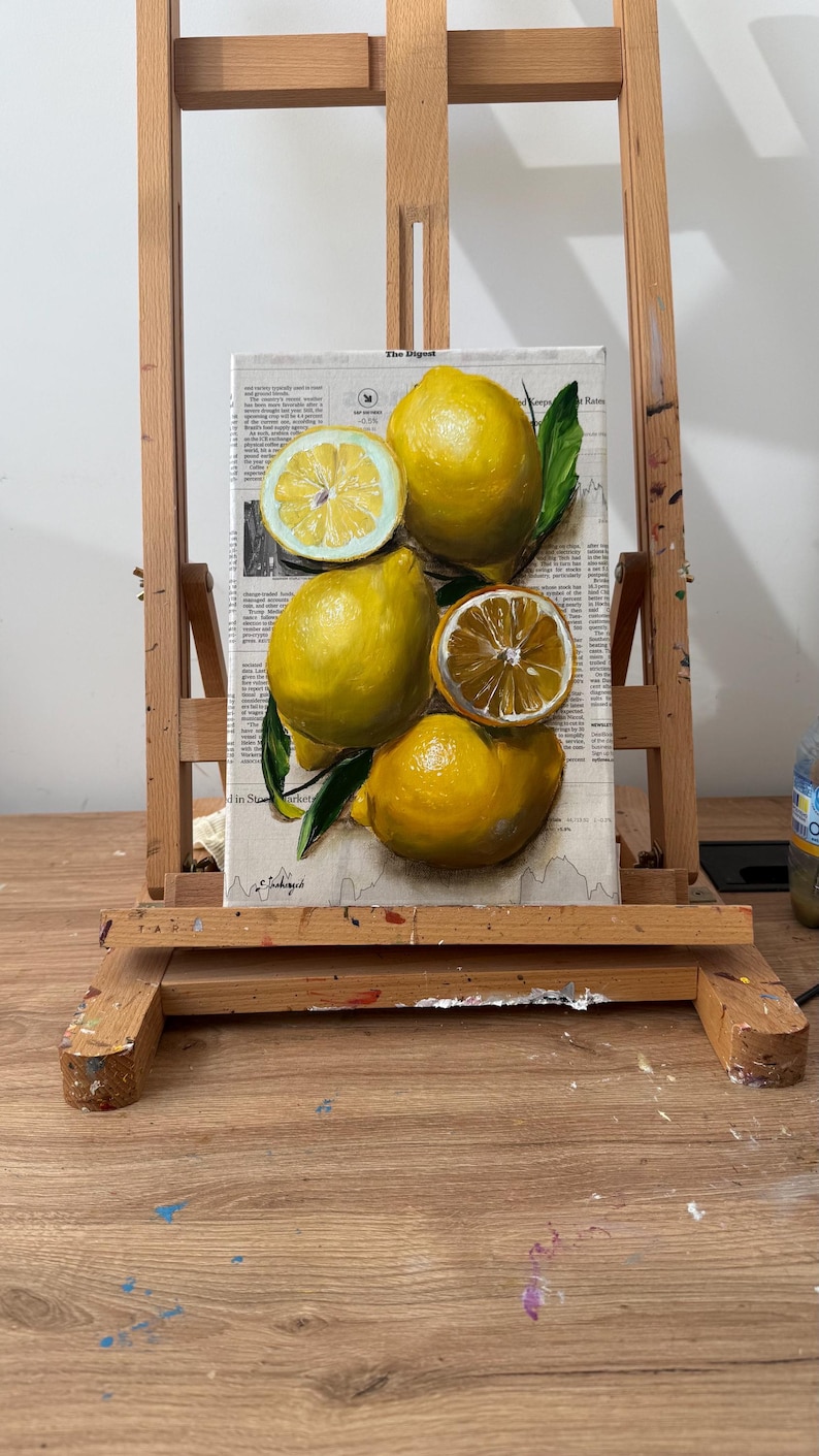 May include: A rectangular canvas painting featuring a cluster of bright yellow lemons, including two whole lemons and two sliced halves, accented with dark green leaves. The artwork is layered over a background of printed newspaper text.