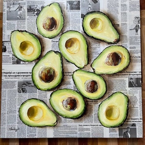 May include: A still life painting of avocados on a newspaper background. The avocados are cut in half and show the green flesh and brown seed. The painting is done in a realistic style with visible brushstrokes.