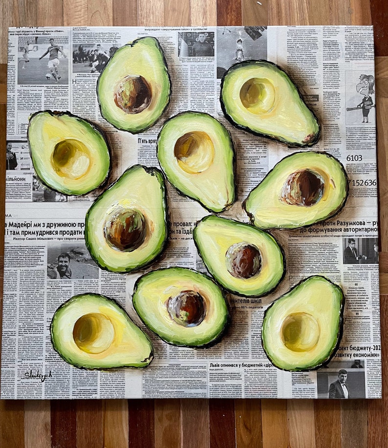 May include: A still life painting of avocados on a newspaper background. The avocados are cut in half and show the green flesh and brown seed. The painting is done in a realistic style with visible brushstrokes.