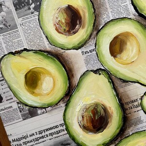 May include: A painting of several avocado halves on a newspaper background. The avocados are painted in a realistic style with green skin and yellow flesh. The newspaper is blurred and unreadable.