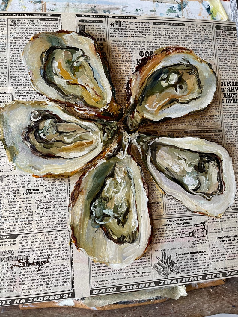 May include: A close-up of five oyster shells painted in shades of brown, white, and green. The shells are arranged in a flower shape on top of a newspaper.