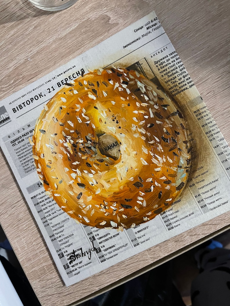 May include: A close-up of a painted bagel with a white center and a yellow outer ring. The bagel is covered in white and black sesame seeds.