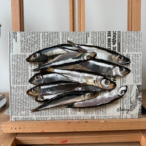 May include: A painting of a group of silver fish on a newspaper background. The fish are arranged in a pile, with their tails overlapping. The newspaper is printed in black and white, and the text is visible. The painting is done in a realistic style, with the fish appearing to be three-dimensional.