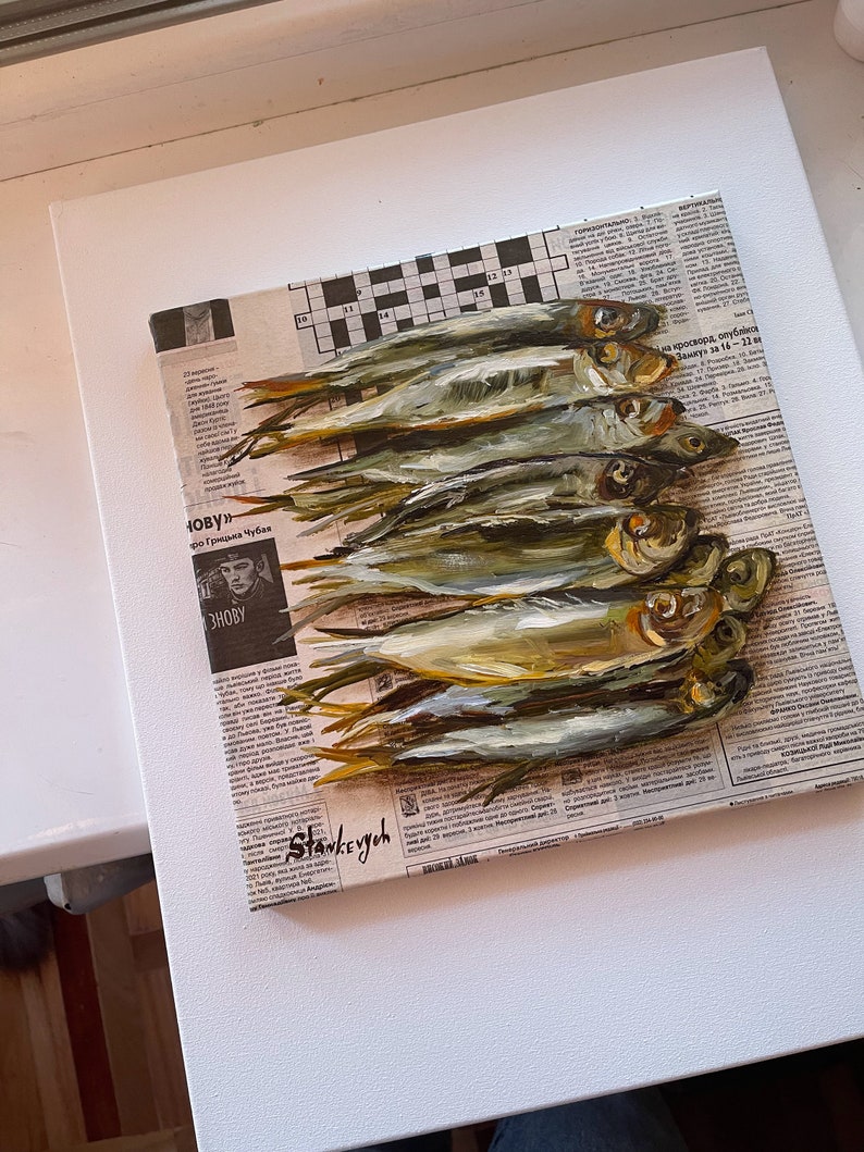 May include: A painting of a still life featuring a pile of silver fish on a newspaper background. The fish are arranged in a row, with their tails pointing to the right. The newspaper is printed in black and white, and the text is visible. The painting is done in a realistic style, with the fish and the newspaper rendered in detail.