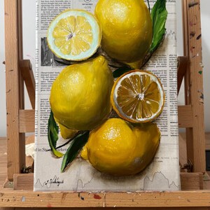 May include: A painting on a canvas featuring bright yellow lemons and green leaves. The composition includes two whole lemons and two halved lemons with visible segments. The background consists of printed newspaper text and columns.