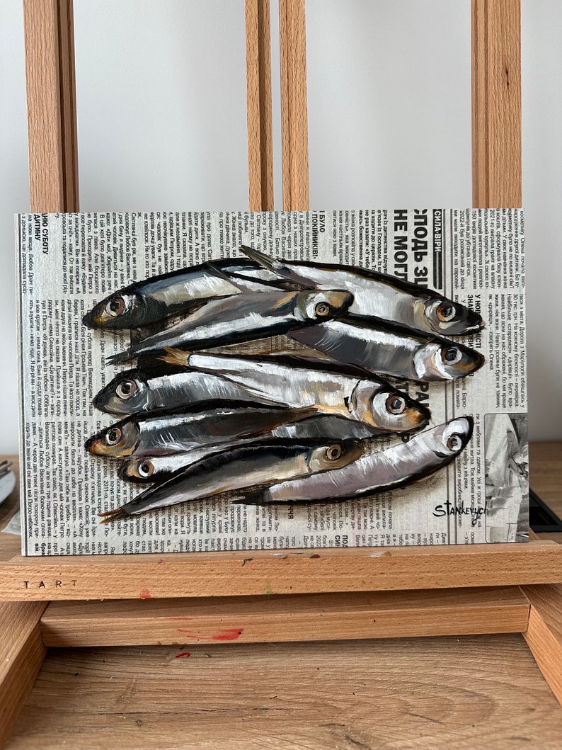 May include: A painting of a group of silver fish on a newspaper background. The newspaper headline reads "Сила віри" and "Злодь ЗЦ НЕ МОГЛ".