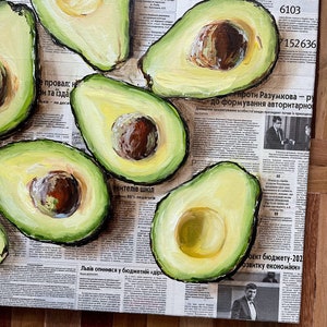 May include: A painting of avocados on a newspaper background. The avocados are painted in a realistic style with green skin and brown pits. The newspaper is printed in black and white and features text in Ukrainian.
