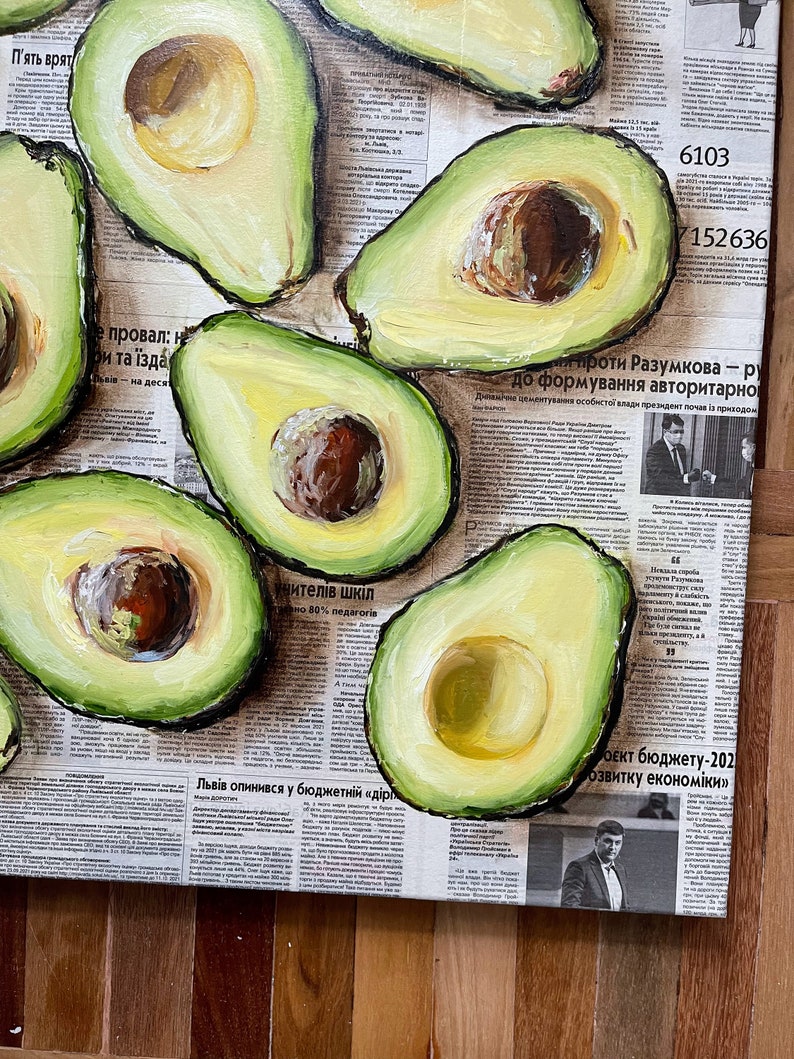 May include: A painting of avocados on a newspaper background. The avocados are painted in a realistic style with green skin and brown pits. The newspaper is printed in black and white and features text in Ukrainian.